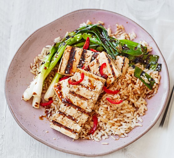 Charred pieces of tofu on a plate with spring onions and rice