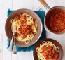 Two bowls of spaghetti topped with bolognese sauce and a pan of extra sauce on the side.